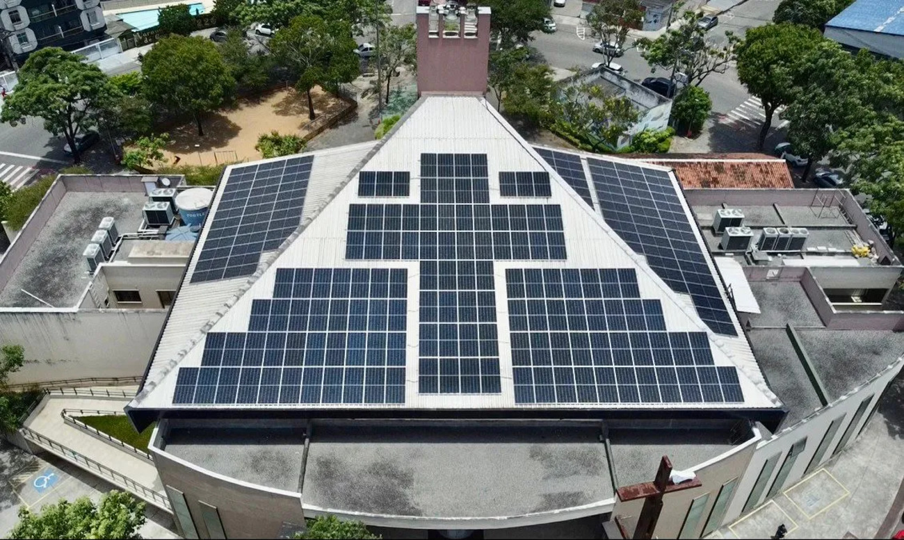 Vista aérea de igreja com telhado coberto por placas solares organizadas em formato de cruz.