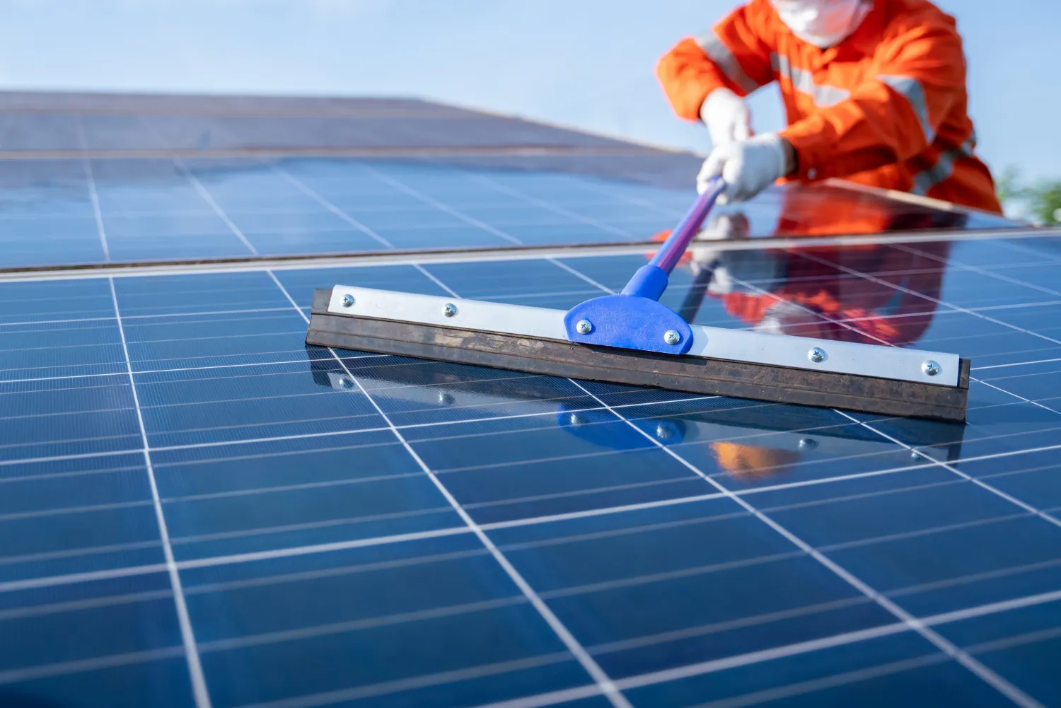 Profissional realizando limpeza de placas solares com rodo em sistema fotovoltaico.