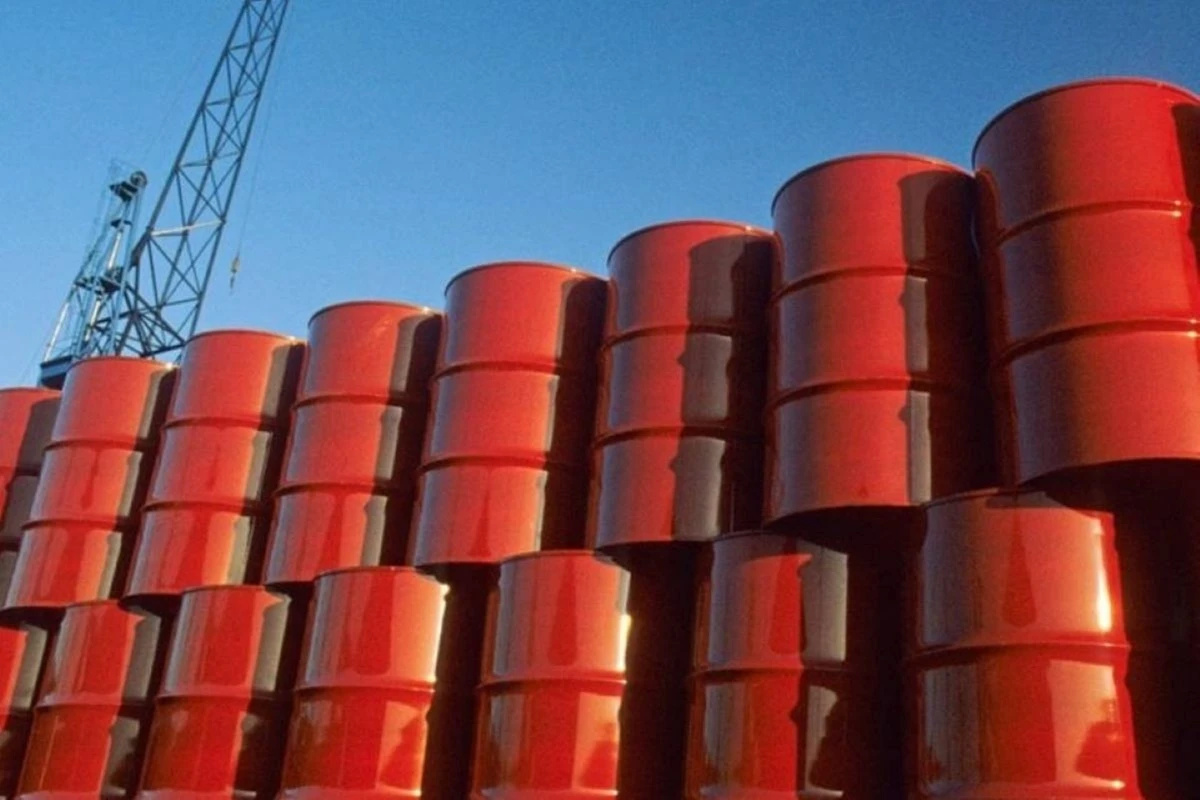 Barris de petróleo empilhados em área industrial com guindaste ao fundo