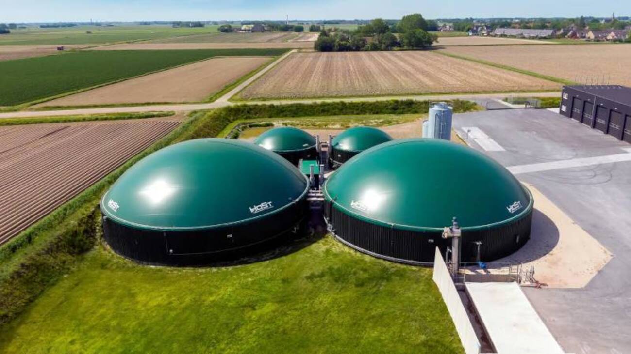 Planta de biogás com grandes biodigestores verdes em área rural cercada por plantações.