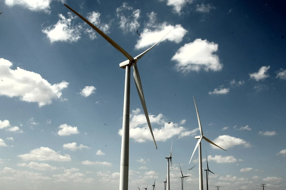 Turbinas eólicas em funcionamento em campo aberto sob céu azul com nuvens, representando geração de energia renovável.