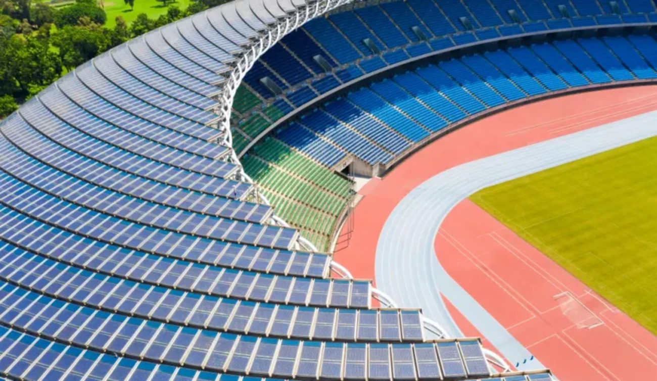 Estádio com cobertura equipada com placas solares ao redor das arquibancadas e pista de atletismo ao centro.