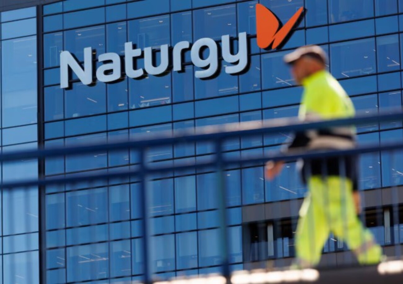 Fachada de prédio corporativo da Naturgy com logotipo em destaque e trabalhador em primeiro plano desfocado.
