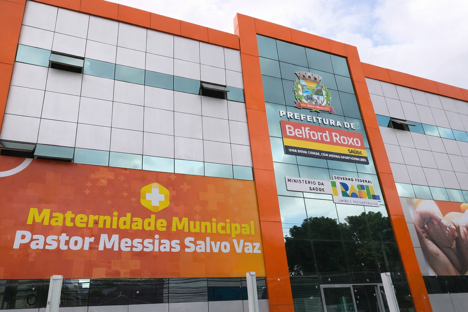 Fachada da maternidade municipal de Belford Roxo com estrutura moderna, cores laranja e branco e identificação da unidade de saúde pública
