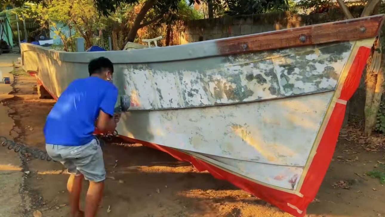 Homem adapta motor automotivo em iate artesanal com sistema náutico funcional, refrigeração externa e casco reforçado.