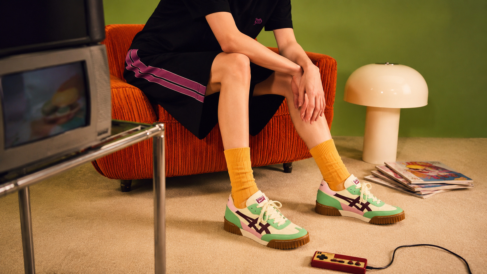 Pessoa usando tênis retrô da Onitsuka Tiger em ambiente de estilo vintage, com poltrona laranja, televisão antiga e decoração inspirada nos anos 1970.
