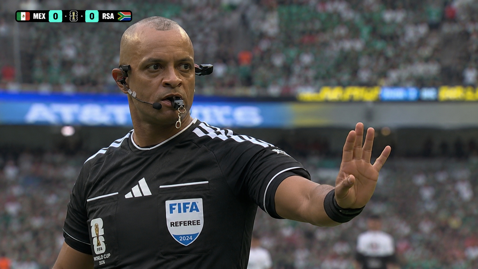 Árbitro brasileiro durante partida da Copa do Mundo de 2026 faz sinalização em campo enquanto conduz México x África do Sul diante de estádio lotado.