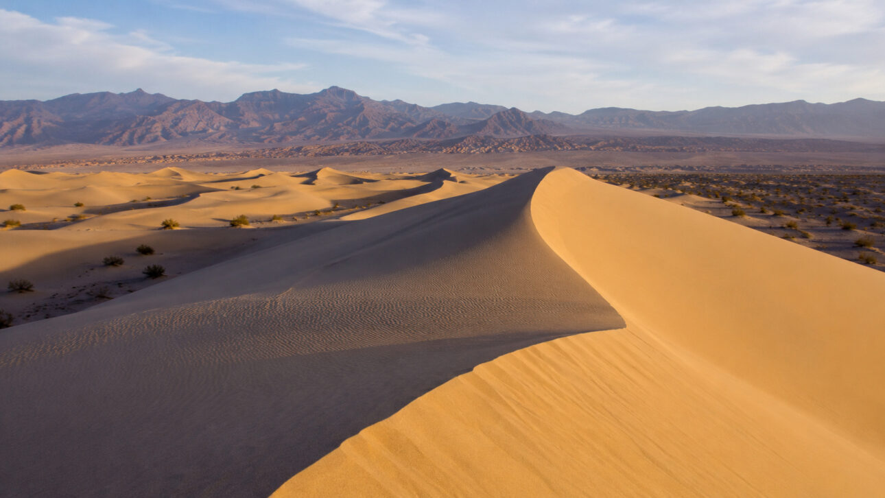 Panoramic view of sand dunes in a desert environment with mountains in the background, representing dry regions and the search for innovative solutions for obtaining drinking water.