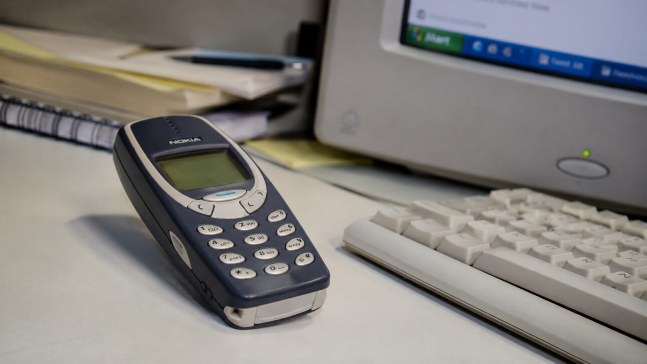 Nokia 3310 phone on a table next to a keyboard and old computer monitor, representing the technology used at the time of Brazil's 2002 World Cup victory.