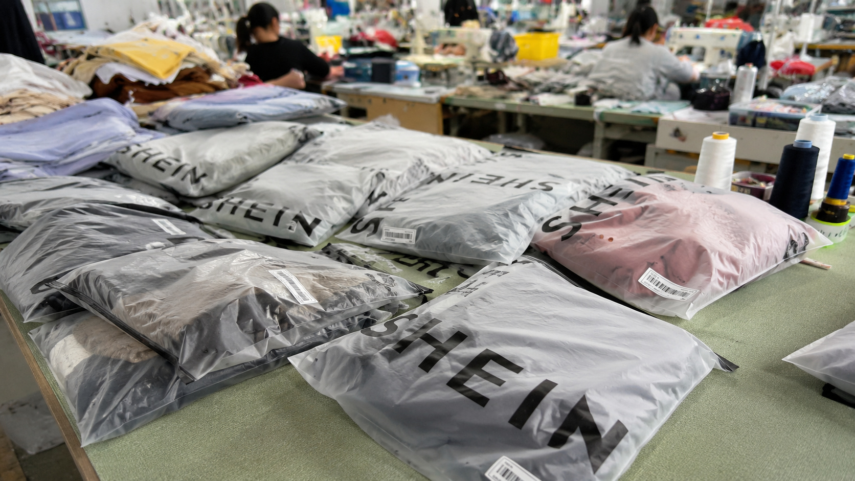 Pacotes de roupas da Shein sobre mesa de separação em ambiente de produção, representando compras internacionais e a volta da taxa das blusinhas em 2027.