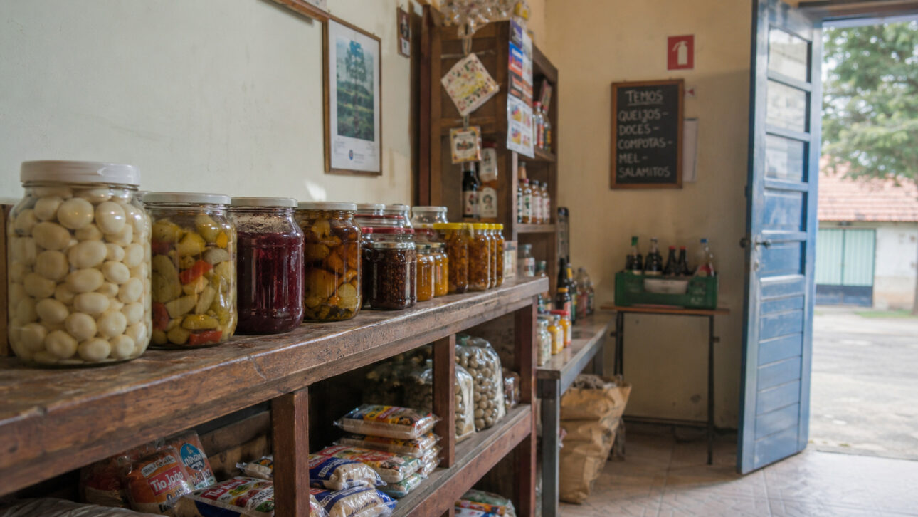 Potes de conservas e produtos artesanais organizados no balcão de madeira de uma vendinha tradicional do interior de São Paulo.