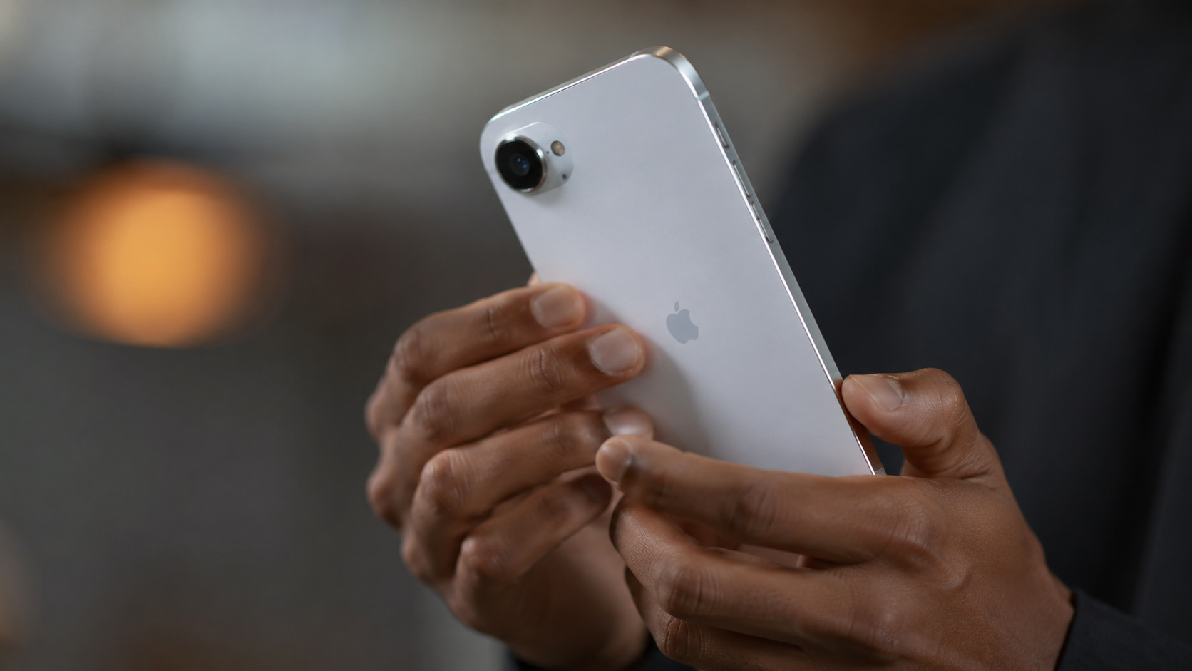 Pessoa segura iPhone branco em referência ao ataque cibernético contra a Tata Electronics e ao vazamento de arquivos sigilosos da Apple.