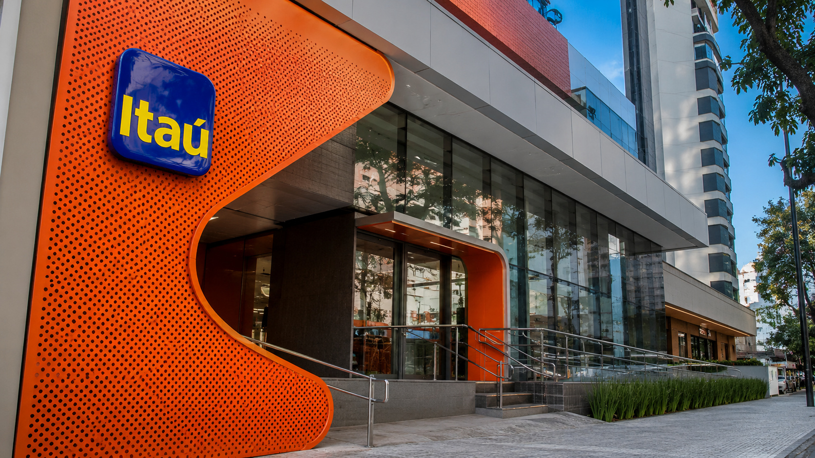 Fachada de unidade do Itaú com logo azul e amarelo, estrutura moderna em vidro e painel laranja, em imagem sobre mudança no trabalho híbrido do banco.