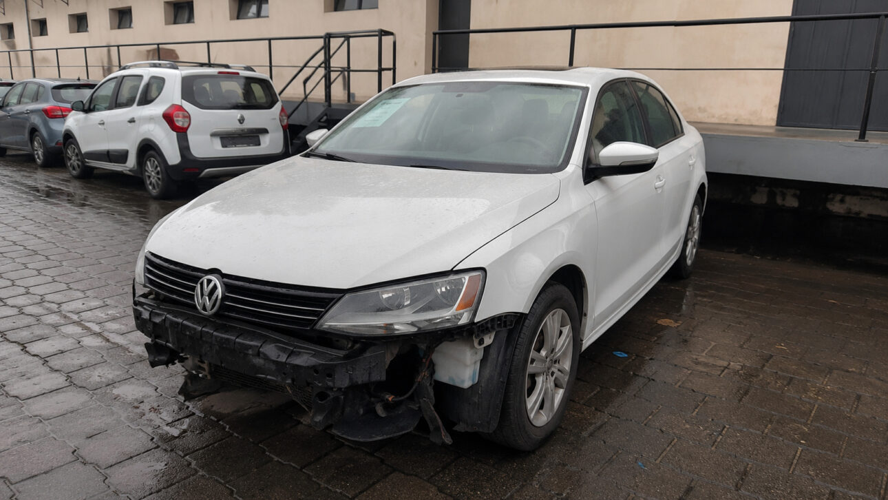 Volkswagen Jetta branco com para-choque dianteiro danificado em pátio, relacionado ao leilão eletrônico da Receita Federal.