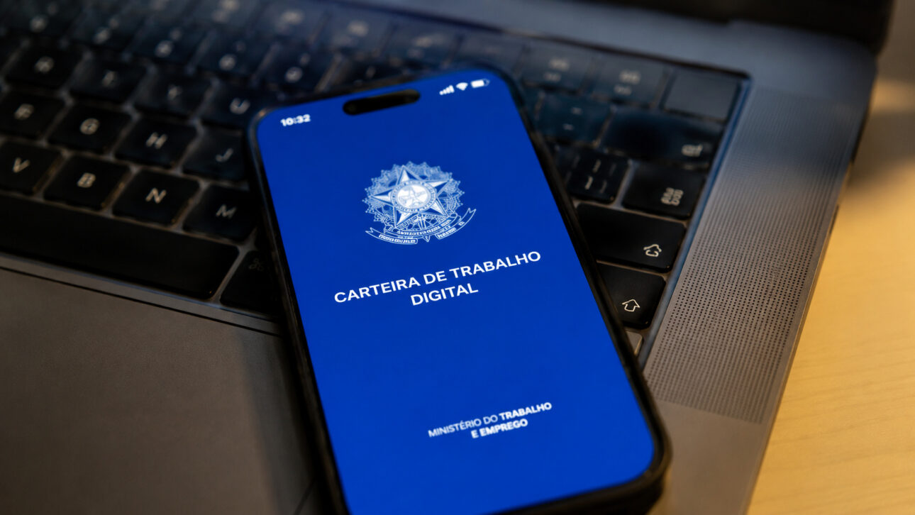 Smartphone with the Digital Work Card screen resting on a computer keyboard, representing access to Consignado CLT.