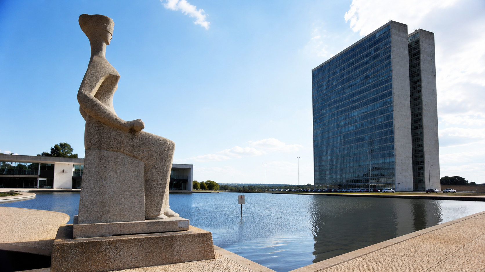 Escultura da Justiça em primeiro plano diante de edifícios do Poder Judiciário em Brasília, representando o debate jurídico sobre a suspensão de resolução do Conanda e a análise do caso pelo STF.