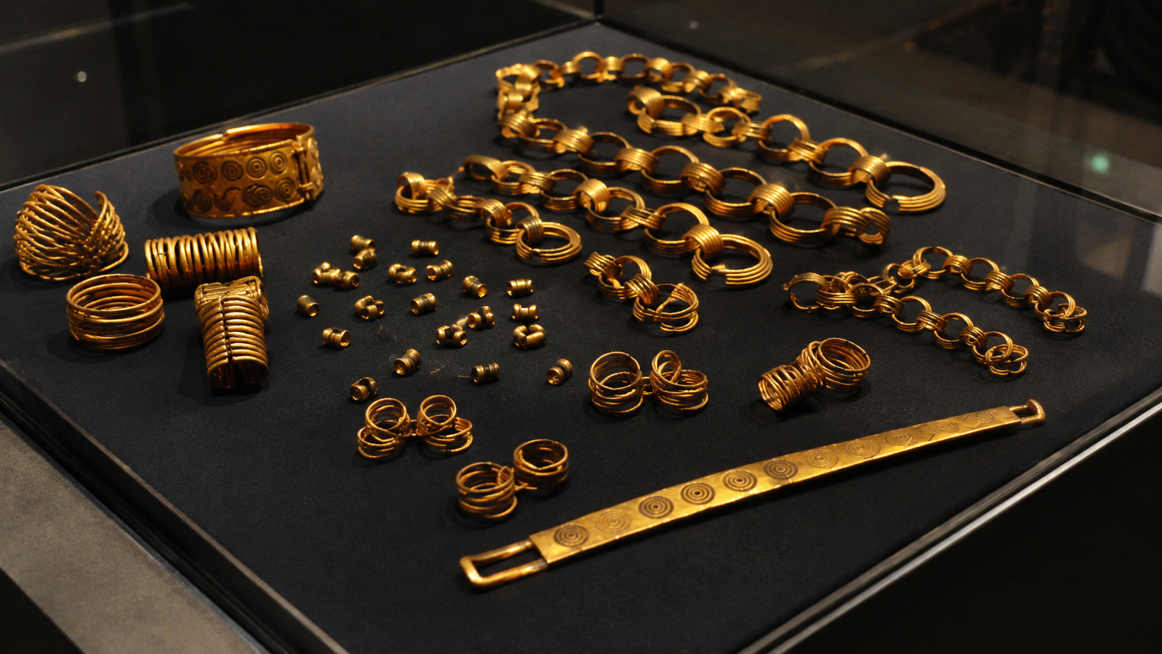 Artefatos de ouro da Idade do Bronze exibidos em vitrine de museu, incluindo correntes espirais, anéis, pulseiras e peças metálicas associadas ao misterioso Tesouro de Gessel encontrado na Alemanha.