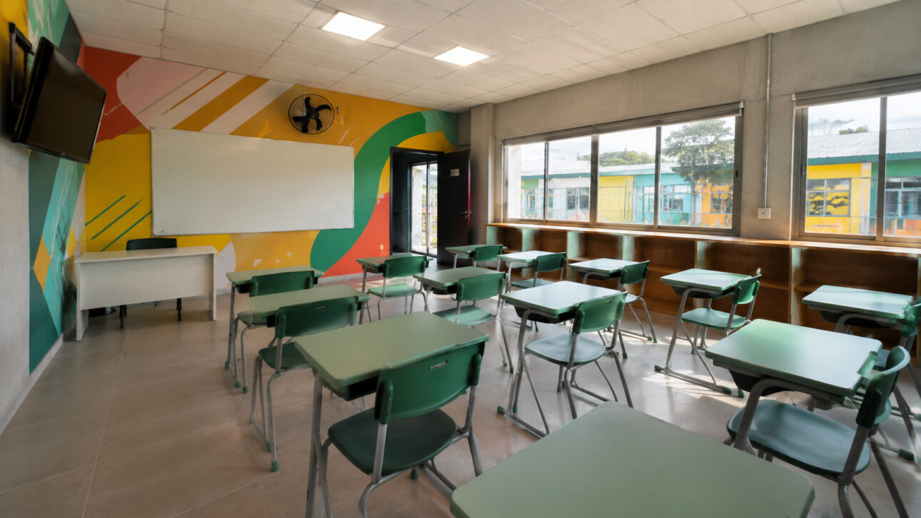 Modern classroom of the School of the Future with organized green desks, colorful mural, whiteboard, large windows, and sustainable furniture produced from the recycling of banknotes discarded by the Mint.