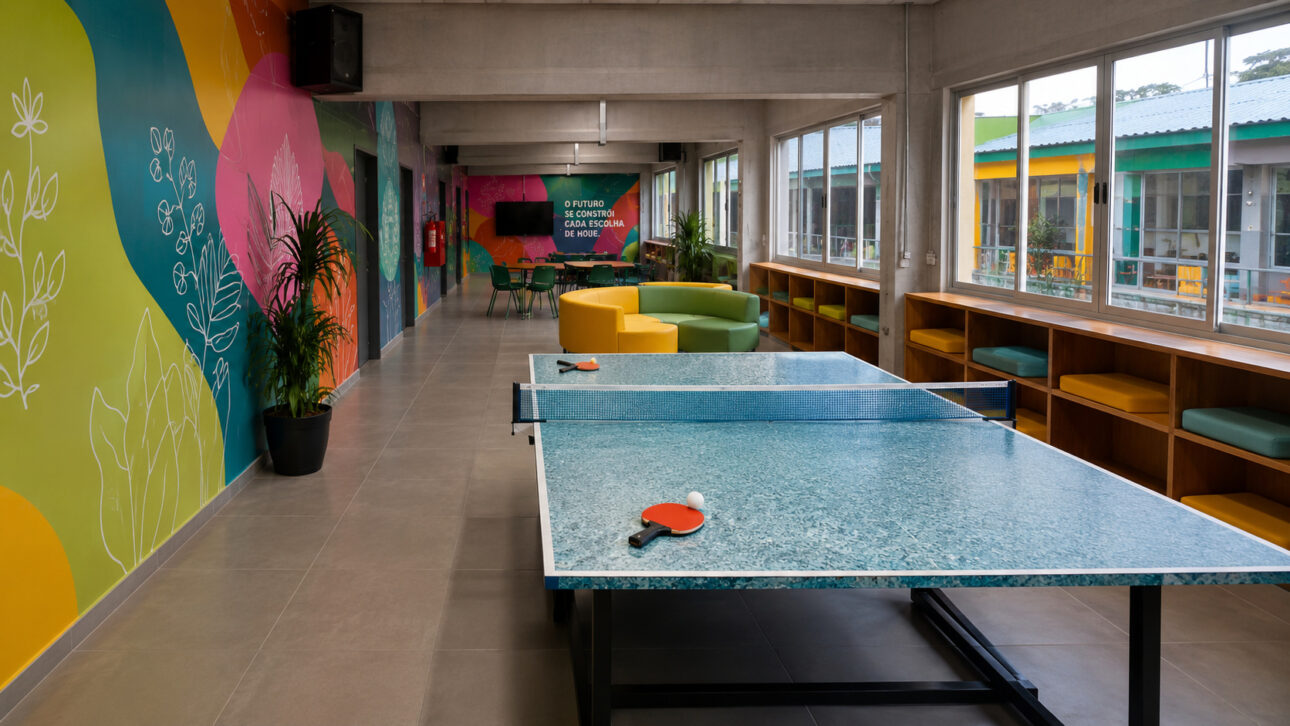 Interior area of the School of the Future with a ping-pong table made from recycled materials, colorful educational mural, sustainable furniture, large windows, and a modern environment focused on the integration between technology, education, and student interaction.