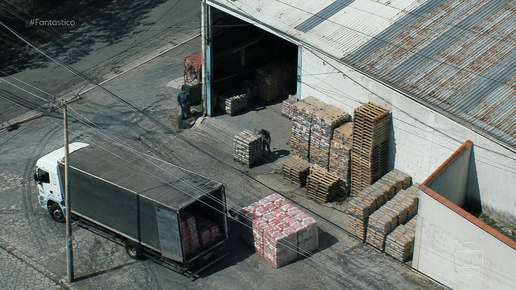 Caminhão realiza carregamento de sacos de farinha em galpão industrial no Rio de Janeiro, cenário que remete à investigação sobre controle de fornecedores por tráfico e milícias.