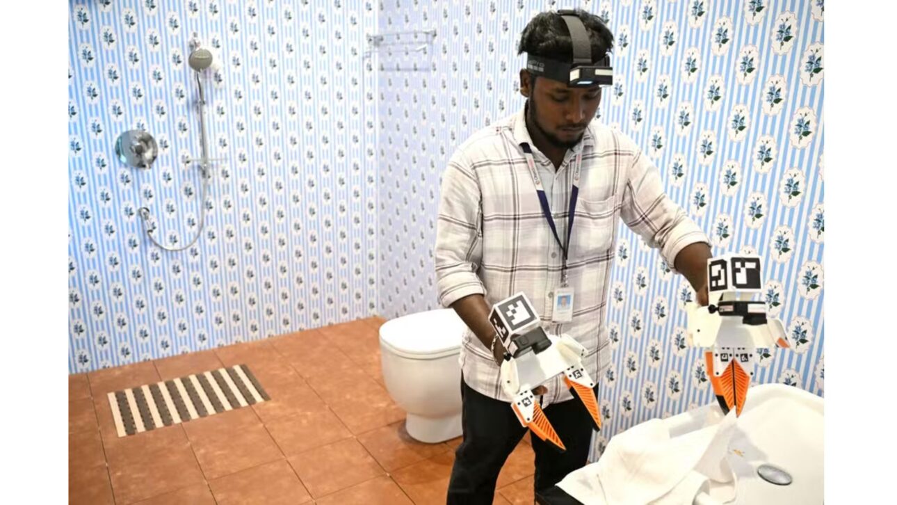 Trabajador con una cámara GoPro en la cabeza, grabando sus acciones mediante captura de movimiento mientras dobla toallas dentro de un baño modelo en la oficina de la empresa de datos — Foto: R.SATISH BABU / AFP