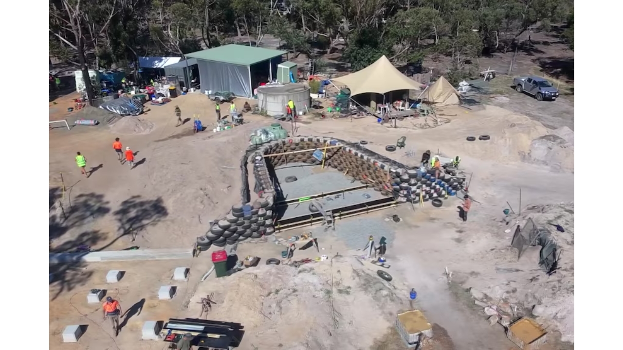 Imagem aérea mostra o canteiro de obras da Earthship em Pomonal, onde 35 trabalhadores chegaram de diferentes regiões para reconstruir o lar destruído pelo incêndio de 2024. A estrutura usa pneus cheios de terra, garrafas e latas reaproveitadas em um projeto sustentável pensado para resistir melhor ao fogo. Crédito: ABC News, Joan Pahissa.