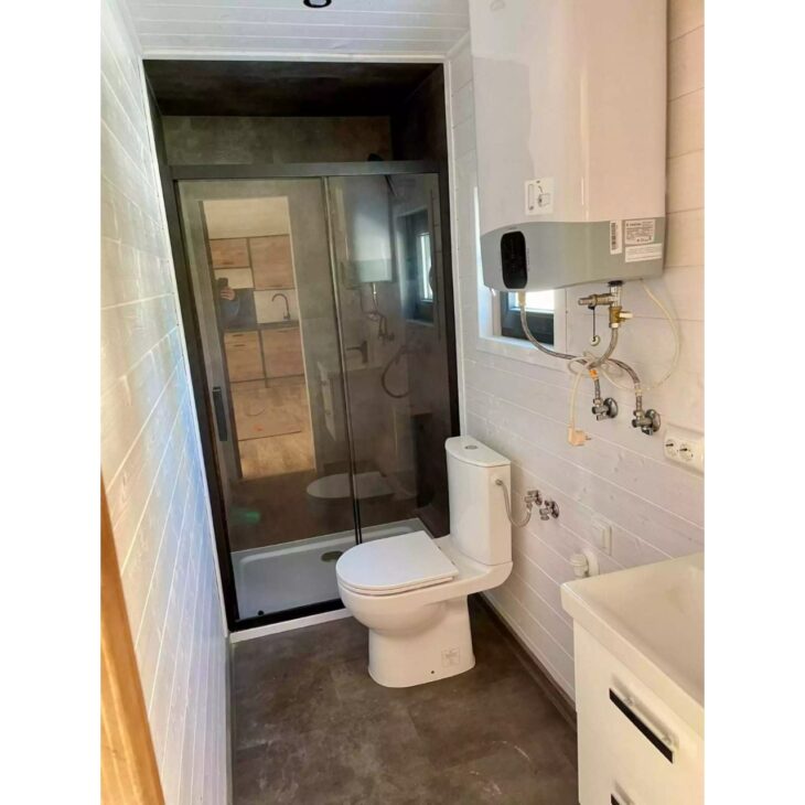 The bathroom of the modular house reinforces the proposal of permanent housing, with a glass shower, flush toilet, installed heater, and compact structure that tries to deliver real comfort within just 35 m².