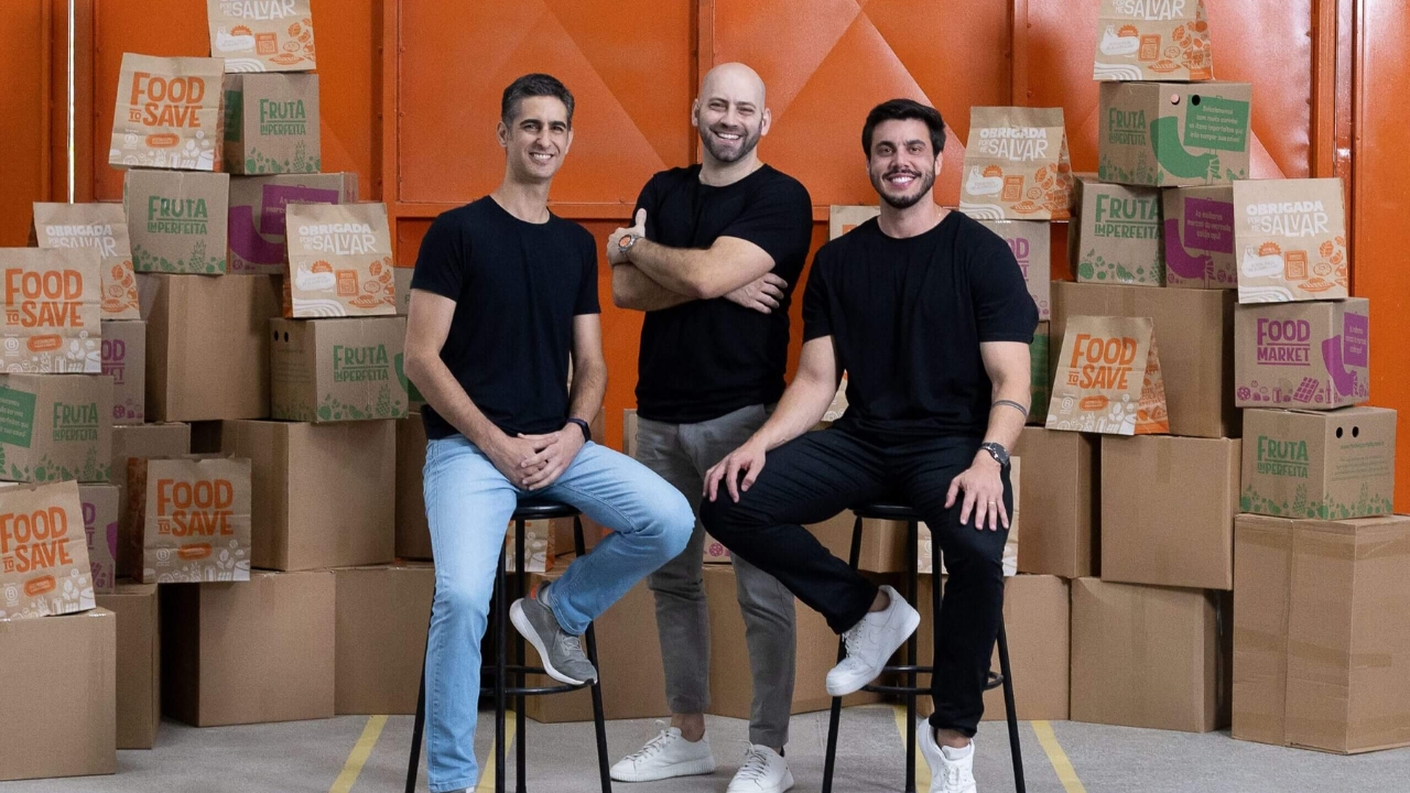 Lucas Infante, Guido Bruzadin Neto e Fernando Reis, da Food To Save, posam entre embalagens da startup, que ganhou escala no Brasil ao vender sacolas surpresa com alimentos próximos do vencimento e excedentes de comércios parceiros.