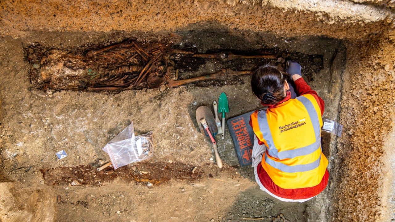 Un esqueleto con siglos de historia emerge centímetro a centímetro bajo las manos de una investigadora del INRAP. Cada sepultura encontrada en la Saint-Philibert lleva información sobre la vida — y la muerte — en la Borgoña medieval — Crédito: Christophe Fouquin / INRAP