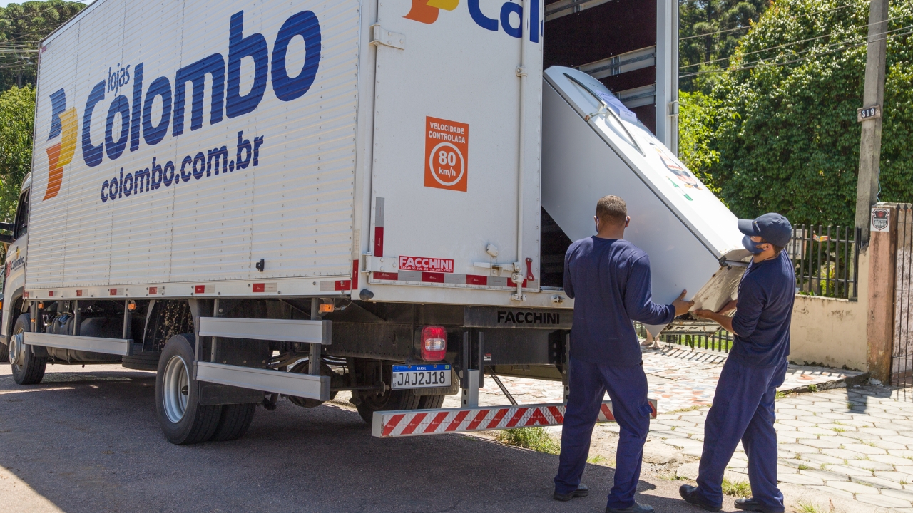 Funcionários carregam refrigerador durante entrega vinculada ao programa Trocou, Economizou, da Copel, que incentiva consumidores do Paraná a substituir geladeiras antigas por modelos mais eficientes, com desconto na compra e recolhimento do aparelho usado.