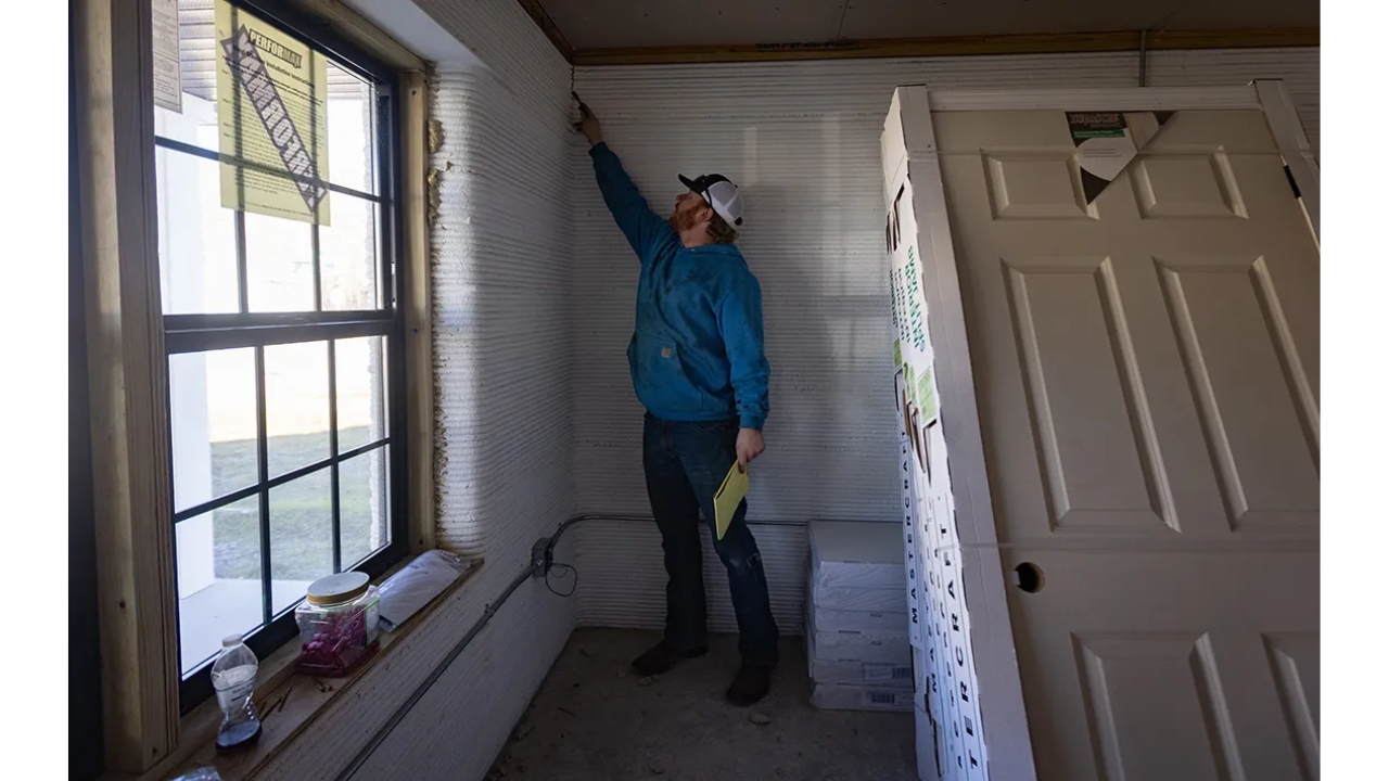 Ryan Moore, then an employee of Prestige, points in December to a crack in the 3D printed duplex. The fissure was one of dozens that, according to the company, led to the work stoppage. Prestige stated that it waited for a year for a repair plan from the printer supplier and, without receiving the solution, ended up using hydraulic cement. Photo: Julia Rendleman.