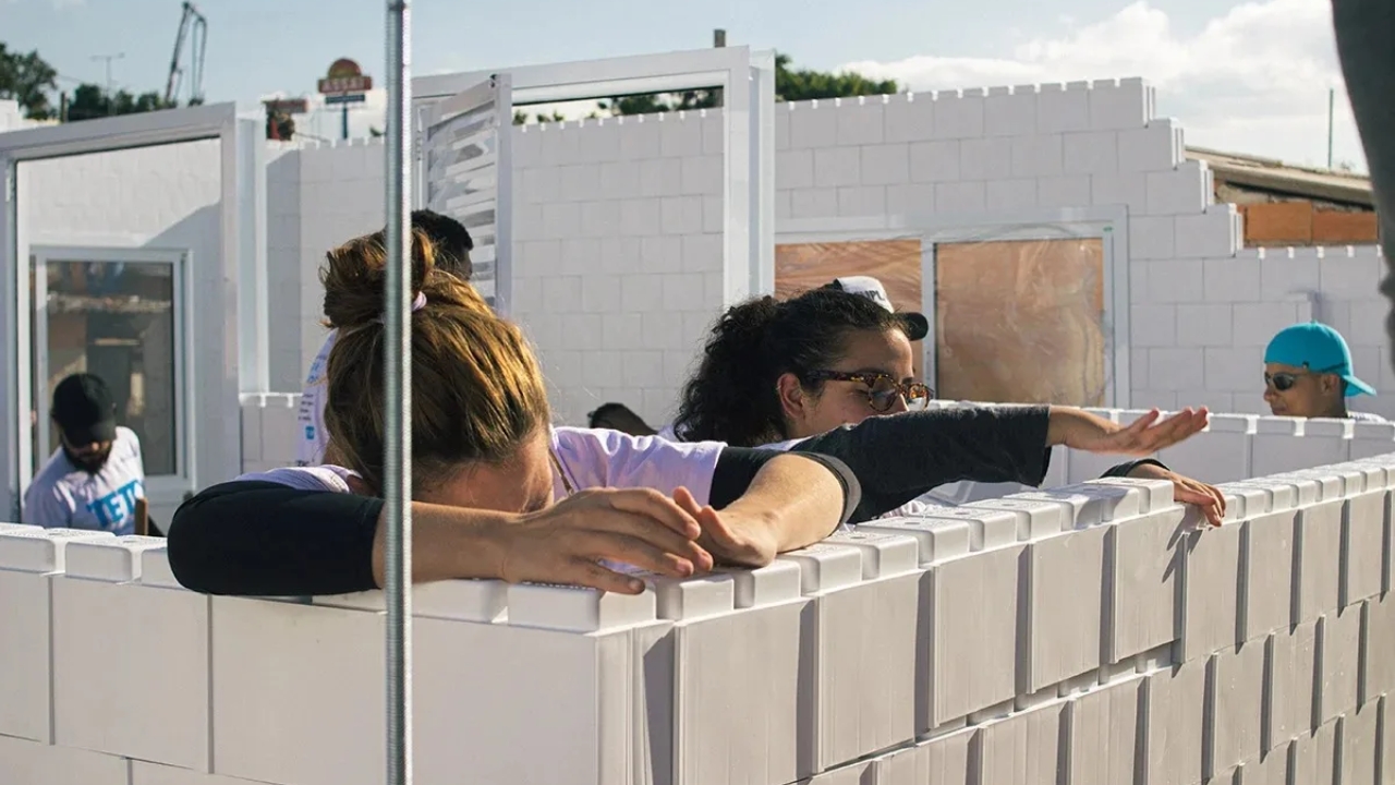Voluntárias participam da montagem da Moradia Semente Eco Sustentável, em São Paulo, usando blocos de plástico reciclado encaixados na estrutura. O sistema modular ajudou a erguer a casa de 27 m² em apenas 15 horas e mostra como resíduos podem virar parede em projetos de moradia social.