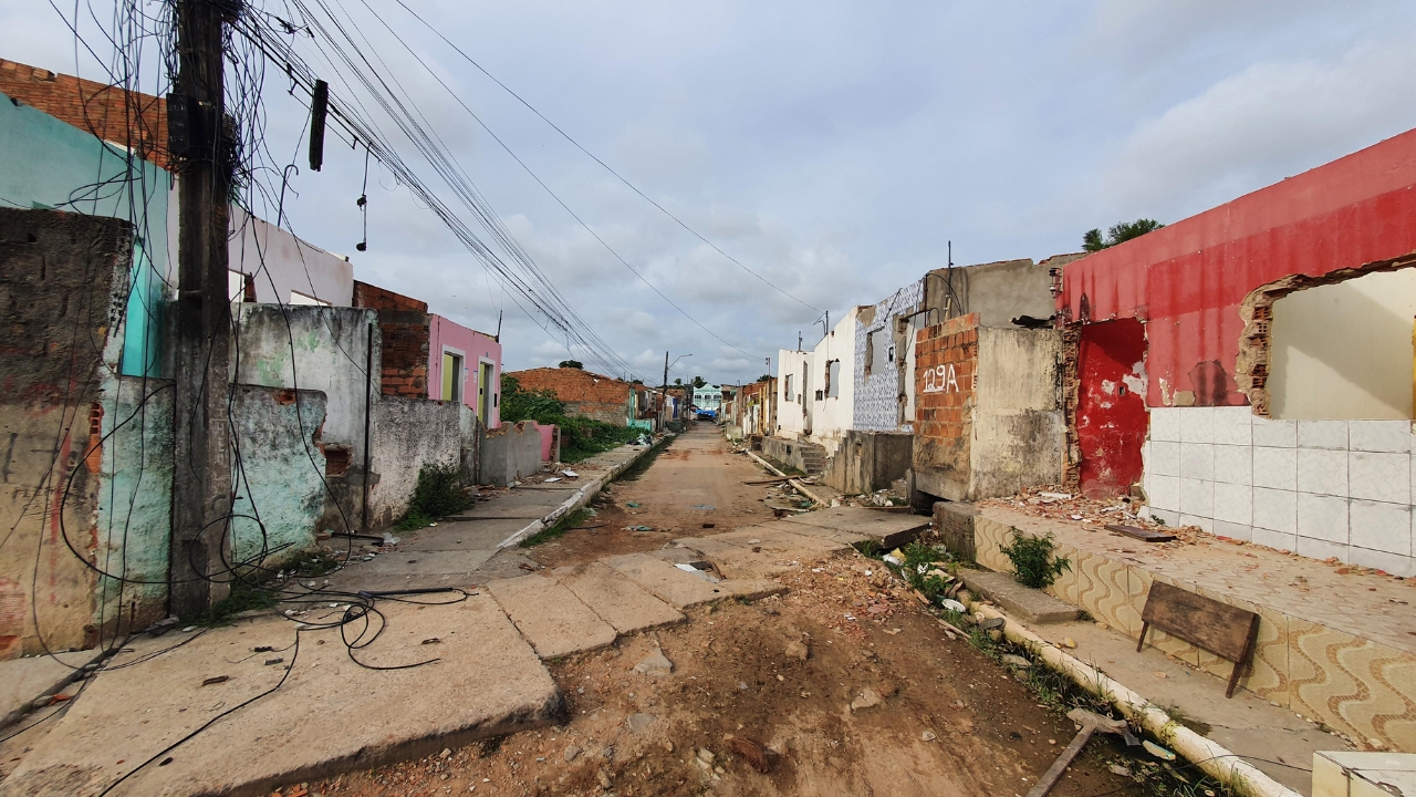 Calle con casas demolidas, estructuras expuestas y señales de abandono muestra el impacto duradero de la crisis causada por el hundimiento del suelo en Maceió, donde barrios enteros perdieron habitantes, comercios y la vida cotidiana tras el avance de la tragedia ligada a la minería de sal-gema.