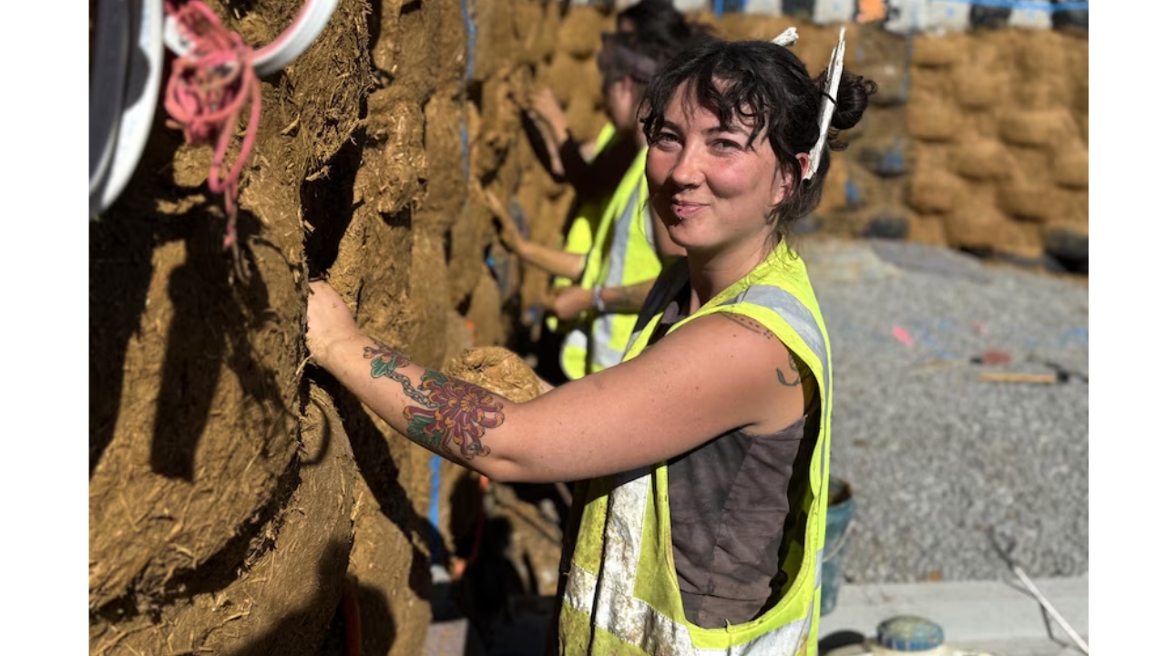 Trabalhadora aplica cob nas paredes da Earthship reconstruída em Pomonal, técnica que mistura barro e fibras naturais sobre uma estrutura feita com pneus, garrafas e latas reaproveitadas. O projeto usa mais de 350 pneus cheios de terra para criar uma moradia mais sustentável e resistente ao fogo. Crédito: ABC News, Eden Hynninen.