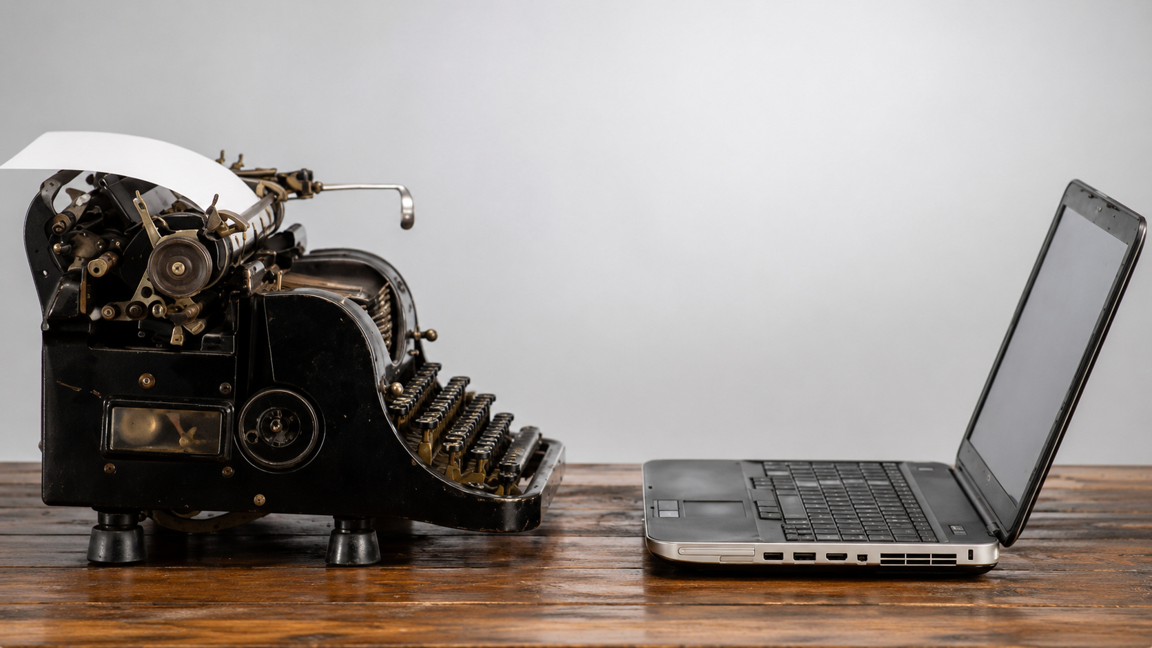 Máquina de escrever antiga posicionada diante de um notebook moderno sobre uma mesa de madeira, representando a evolução do trabalho, das ferramentas profissionais e das diferentes gerações no mercado de trabalho.