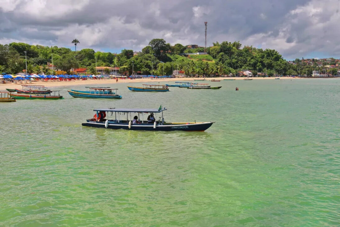 Embarcações navegam próximas à praia de São Tomé de Paripe, em Salvador, região afetada por contaminação química que motivou decreto de emergência ambiental e gerou impactos para pescadores e moradores locais.