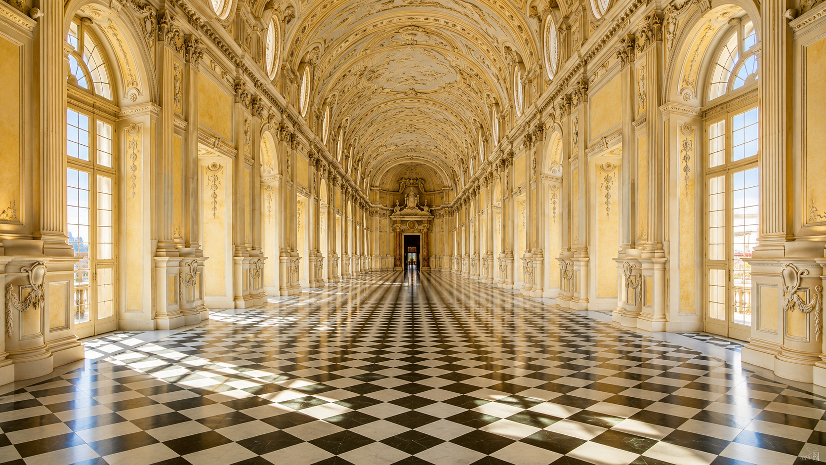 Galeria Grande da Reggia di Venaria Reale com arquitetura barroca, piso xadrez preto e branco, janelas monumentais e decoração histórica restaurada no Piemonte, Itália.