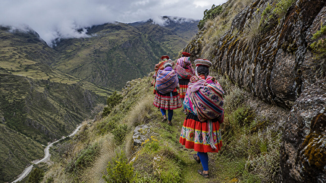 Andean indigenous women in traditional clothing walk along a mountain trail in the Peruvian Andes.
