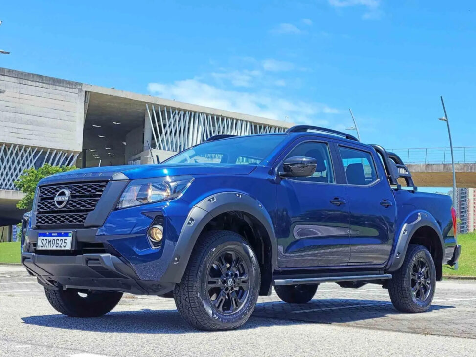 Nissan Frontier Attack 2026 blue parked in an urban area, highlighting black grille, widened fenders, 17-inch wheels and robust look of Nissan's mid-size pickup.