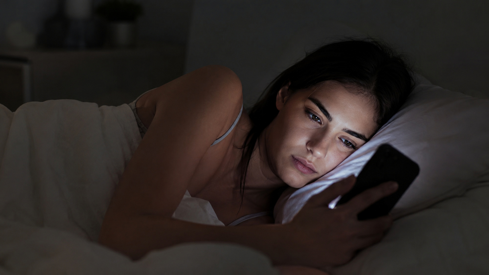 Pessoa usando celular à noite enquanto redes sociais e notificações simbolizam o vício em celular e o excesso de tempo de tela.