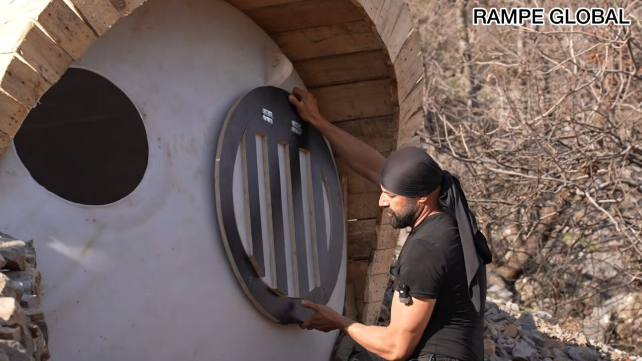 Repurposed water tank turns into a hobbit-style house with pallets, semi-buried structure, and curved facade in a project that combines recycling, low cost, and thermal insulation.