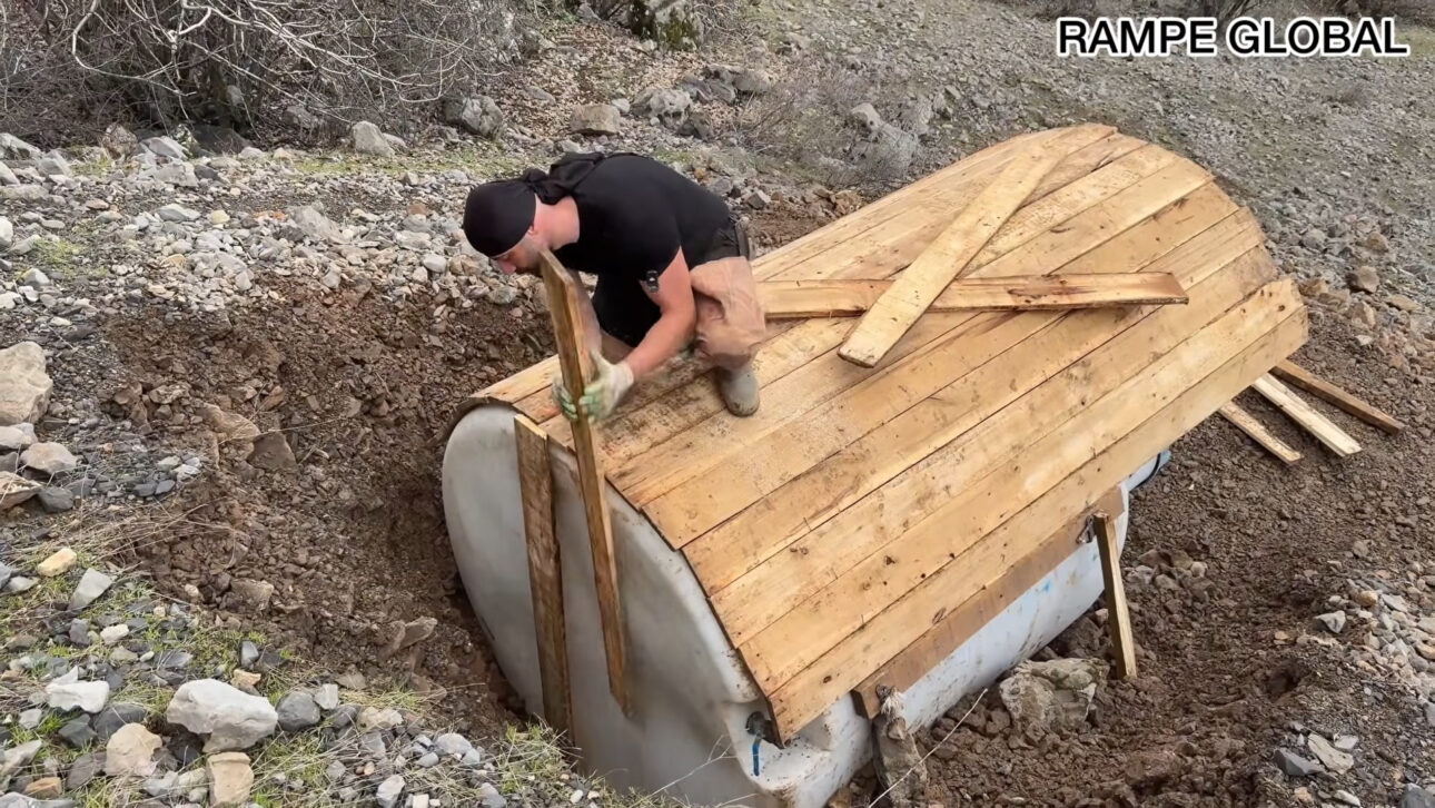 Reused water tank becomes a hobbit-style house with pallets, semi-buried structure, and curved facade in a project that combines recycling, low cost, and thermal insulation.