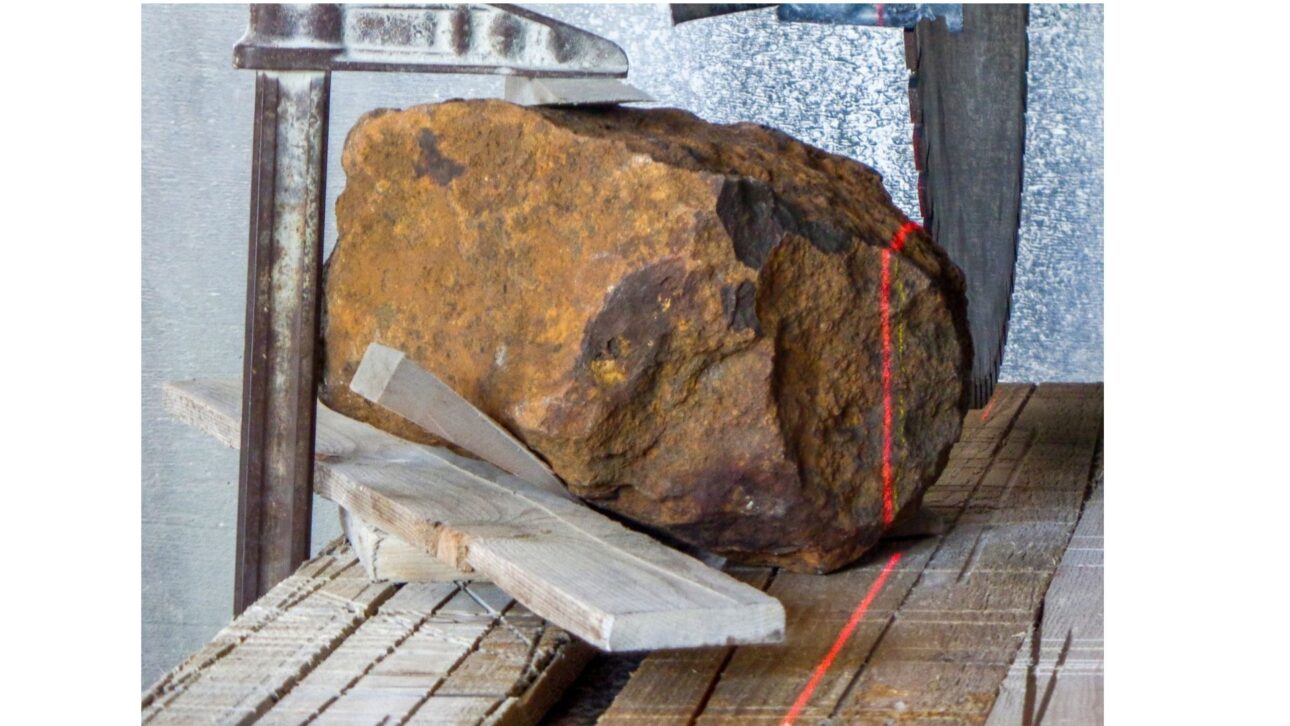 Serra de pedra guiada a laser – a abertura de ‘Blaubeuren’. A remoção da seção do canto, que seria cortada do meteorito ‘Blaubeuren’ com uma serra diamantada, foi primeiro simulada com um gabarito e, em seguida, a peça foi fixada no dispositivo de serragem. Um laser foi então usado para confirmar se o meteorito estava na posição desejada no plano de corte, antes que a serra diamantada cortasse ‘Blaubeuren’ no plano marcado pelo laser. Imagem: 5/8, Crédito: Gabriele Heinlein