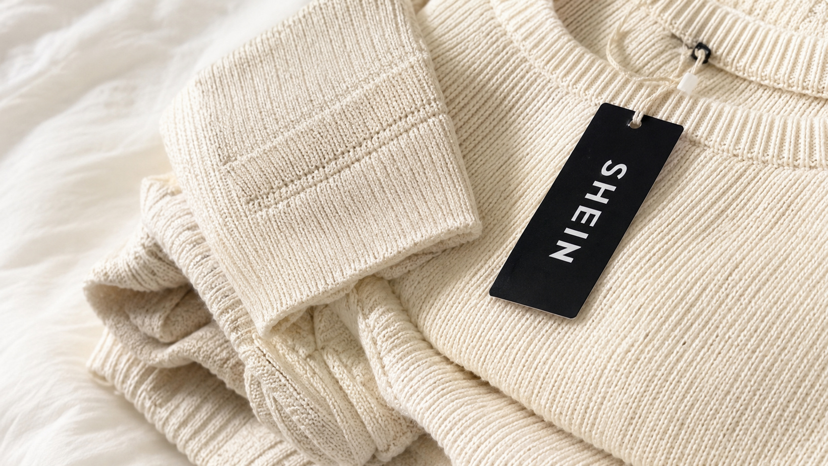 Peças de tricô claras com etiqueta da Shein, plataforma afetada pela nova taxa europeia sobre compras internacionais.