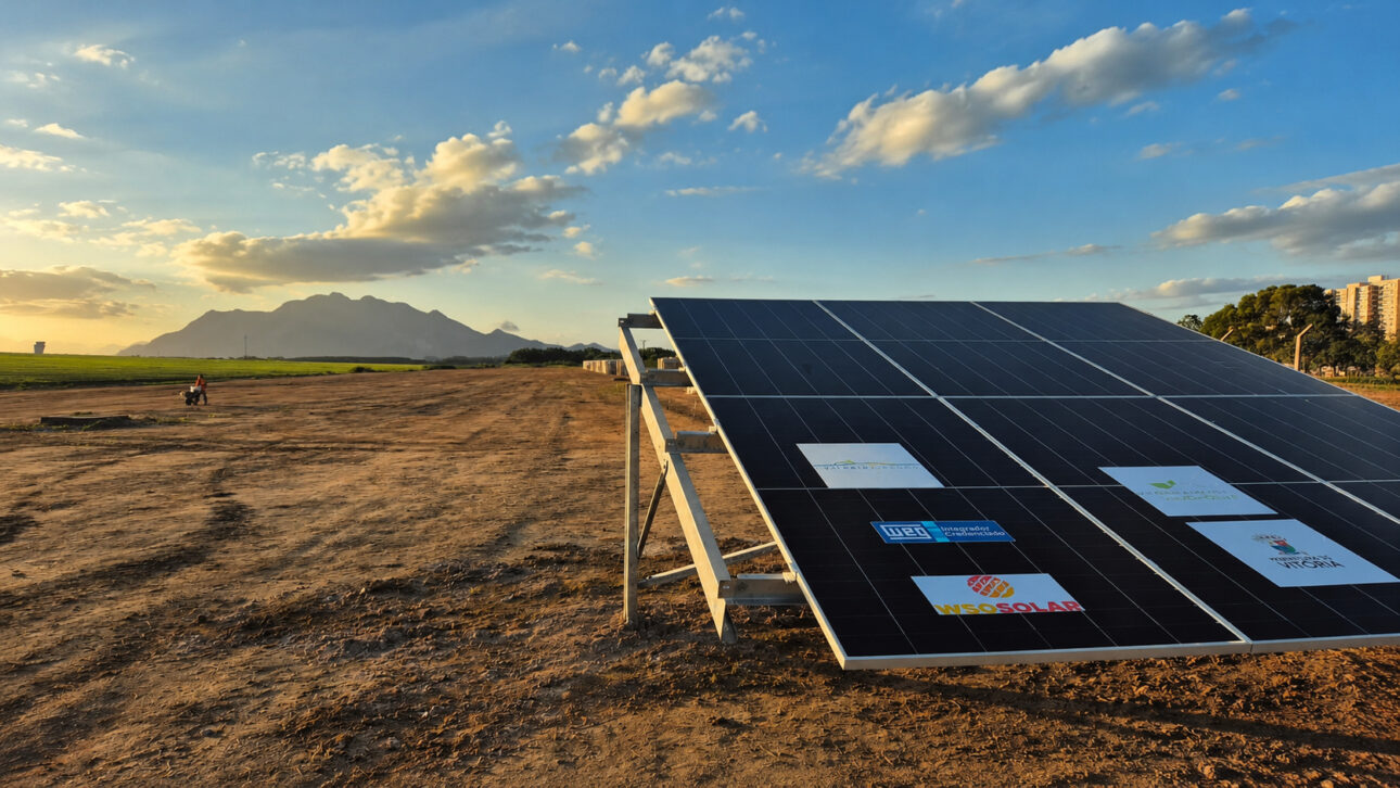 Painéis solares instalados em área do Aeroporto de Vitória durante o pôr do sol, com montanhas ao fundo, representando o avanço do projeto de geração de energia limpa no Espírito Santo.