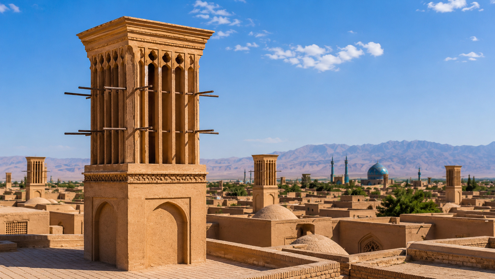 Torre de vento badgir em cidade desértica, com construções de adobe, cúpulas e montanhas ao fundo.