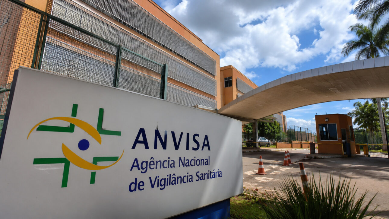 Fachada da Anvisa com placa da Agência Nacional de Vigilância Sanitária em frente ao prédio institucional.