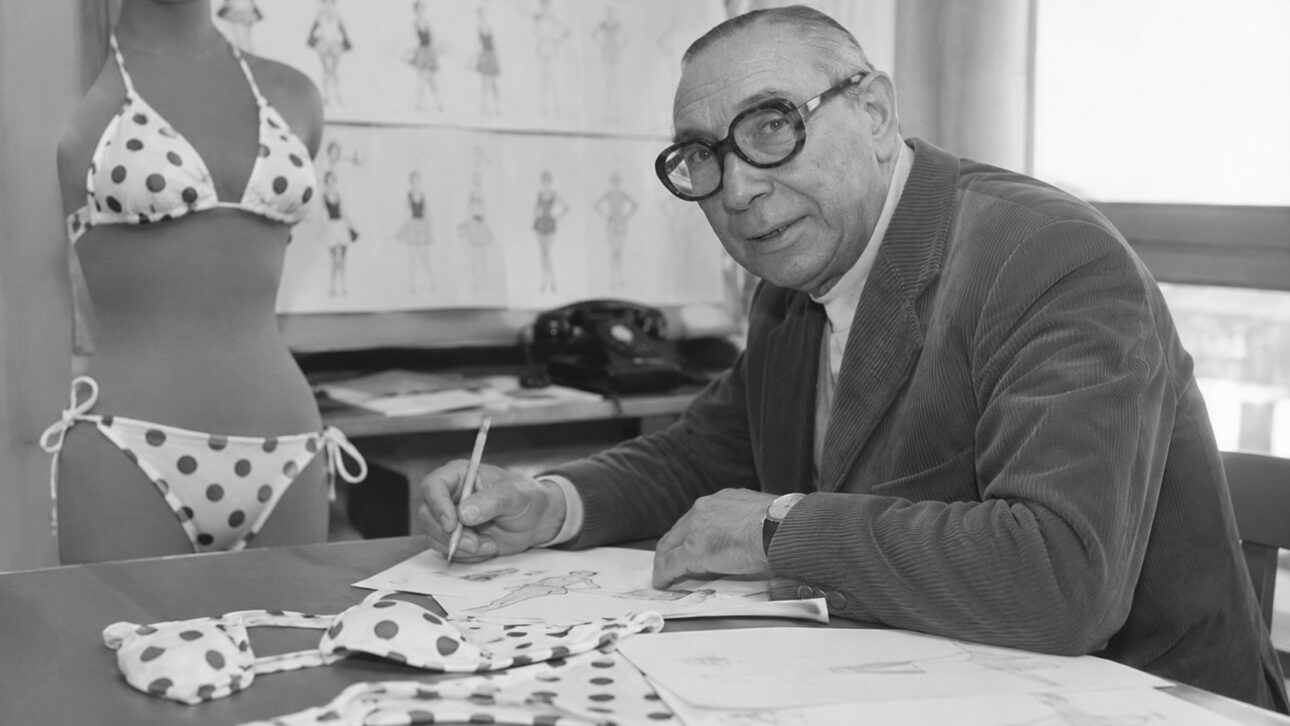 Imagem em preto e branco de Louis Réard desenhando em seu estúdio de moda, ao lado de um manequim vestindo um dos primeiros modelos de biquíni de bolinhas, símbolo da criação da peça que transformou a moda de praia mundial.