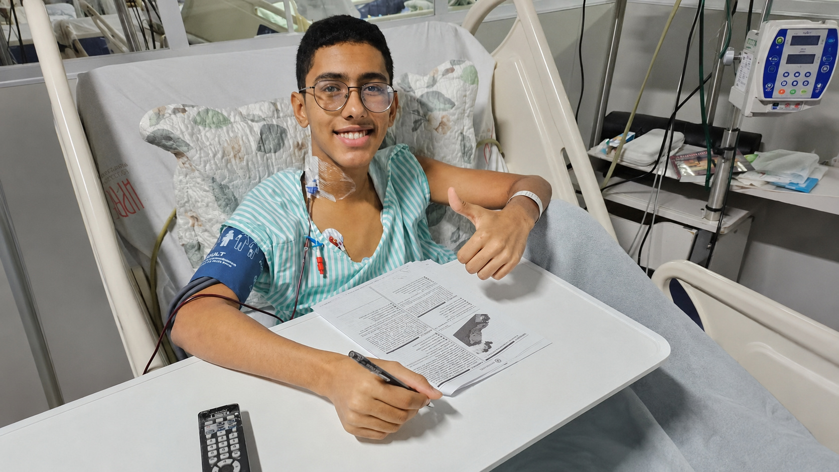 Ítalo Cantanhede no leito hospitalar, com uma prova e uma caneta sobre a mesa, enquanto faz um gesto positivo com a mão.