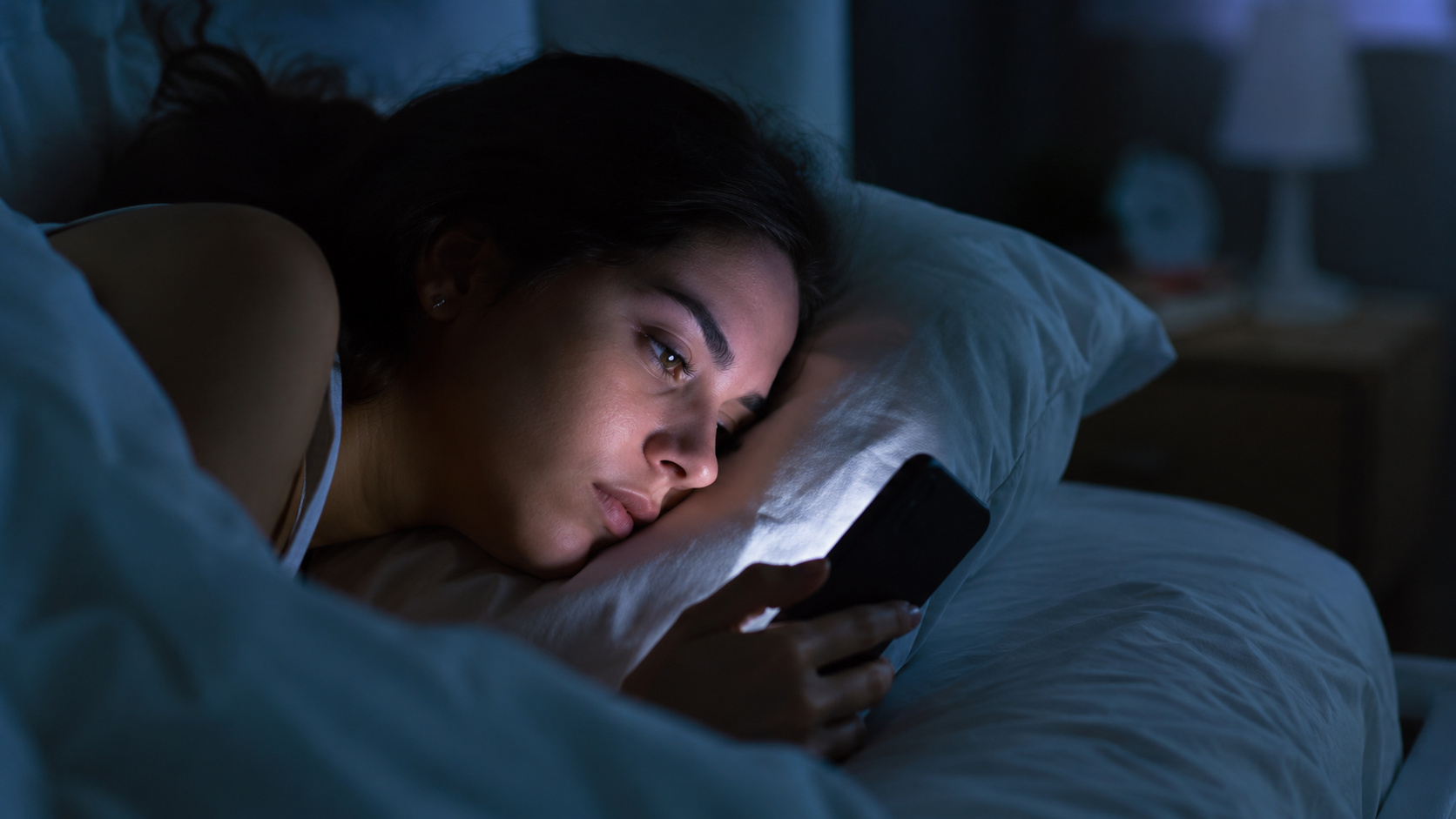 Pessoa utilizando o celular na cama antes de dormir, ilustrando os efeitos da hiperestimulação tecnológica e do uso excessivo de telas na saúde cognitiva.